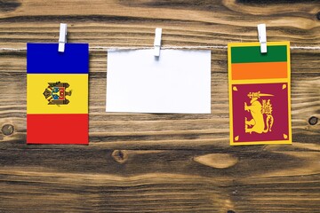 Hanging flags of Moldova and Sri Lanka attached to rope with clothes pins with copy space on white note paper on wooden background.Diplomatic relations between countries.