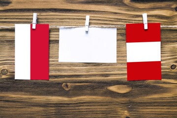 Hanging flags of Monaco and Peru attached to rope with clothes pins with copy space on white note paper on wooden background.Diplomatic relations between countries.