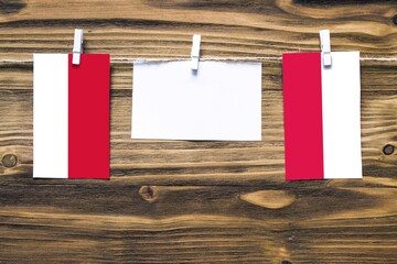 Hanging flags of Monaco and Poland attached to rope with clothes pins with copy space on white note paper on wooden background.Diplomatic relations between countries.