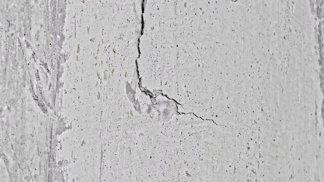 Drill makes a crack in concrete wall and then breaks through the wall, showering plaster.