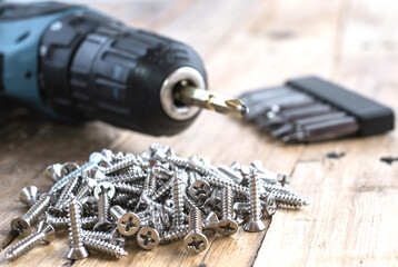 Pile of screws, electric drill with screwdriver bit drill on wooden top table background.
