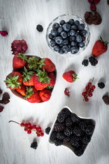 Fresh berry fruits (blackberries, strawberries, blueberries)  in bowls on a white table, shallow depth of field