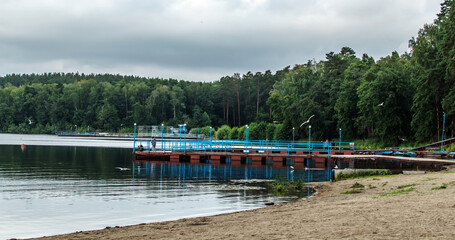 lake shore in a wooded area. cloudy weather. sandy beach. pontoons seagulls