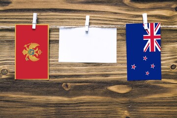 Hanging flags of Montenegro and New Zealand attached to rope with clothes pins with copy space on white note paper on wooden background.Diplomatic relations between countries.