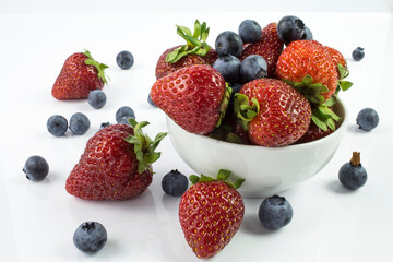 Composition of berries (strawberries, blueberries), fruit in a bowl on a white background with reflection.