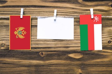 Hanging flags of Montenegro and Oman attached to rope with clothes pins with copy space on white note paper on wooden background.Diplomatic relations between countries.