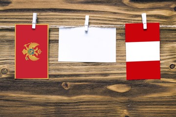 Hanging flags of Montenegro and Peru attached to rope with clothes pins with copy space on white note paper on wooden background.Diplomatic relations between countries.