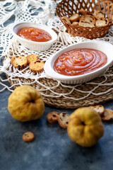 Homemade jelly quince in a white crockery containers with some quince fruits and little toasts to spread.