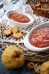 Homemade jelly quince in a white crockery containers with some quince fruits and little toasts to spread.