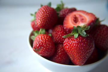 Fresh strawberries  in a white bowl on a white table, shallow depth of field