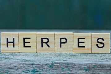 the word herpes from wooden letters on a gray table on a green background