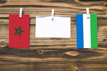 Hanging flags of Morocco and Sierra Leone attached to rope with clothes pins with copy space on white note paper on wooden background.Diplomatic relations between countries.