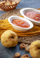 Homemade jelly quince in a white crockery containers with some quince fruits and little toasts to spread.