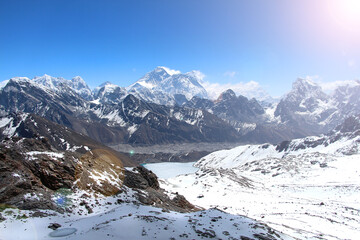 View of Everest mountain peak from the top of Renjo La Pass in Himalayas in sunny day. Everest rises above Lake Gokyo and the village of the same name. Clouds lies on the mountainside.