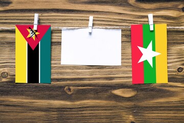 Hanging flags of Mozambique and Myanmar attached to rope with clothes pins with copy space on white...