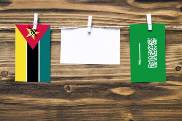 Hanging flags of Mozambique and Saudi Arabia attached to rope with clothes pins with copy space on...