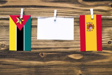 Hanging flags of Mozambique and Spain attached to rope with clothes pins with copy space on white...