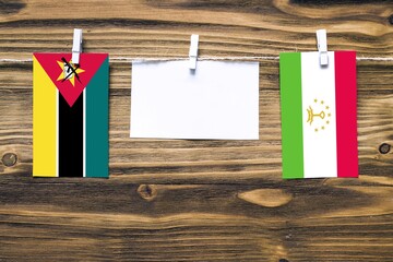 Hanging flags of Mozambique and Tajikistan attached to rope with clothes pins with copy space on...