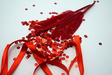 Red sequins, red ribbon and red feathers on white background. Sewing and decorating accessories used for embellishment of dresses