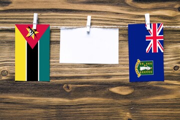 Hanging flags of Mozambique and British Virgin Islands attached to rope with clothes pins with copy space on white note paper on wooden background.Diplomatic relations between countries.