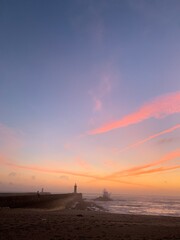 sunset at the pier with the sea lighthouse and the water hitting the rocks
