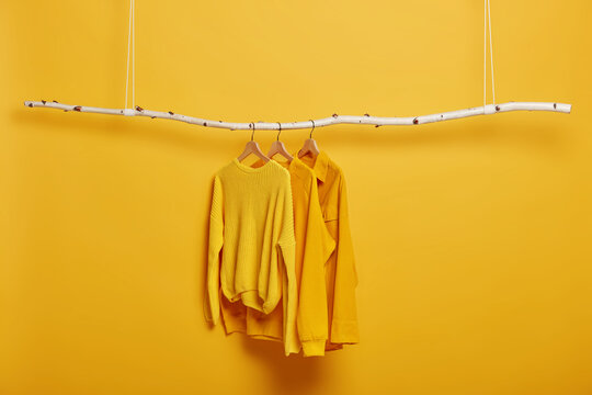 Selective focus. Three items of clothes on hangers. Long sleeved yellow jumpers on wooden rack near bright vivid wall. Copy space for text. Various casual outfits hanging in row at dressing room