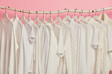 White solid clothes hanging in one row on wooden racks against pink background. Big choice for...