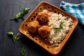 Mexican meatballs with red sauce and rice on dark background