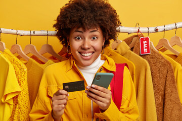 Pleasant looking Afro woman verifies bank account, pays online via smartphone, holds credit card,...