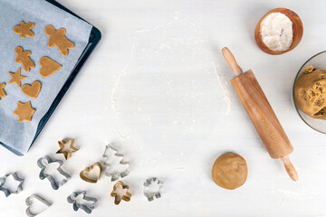 Gingerbread baking concept with gingerbread dough, flour, rolling pin and gingerbread cookies on baking tray.  Copy space for text on white kitchen table.