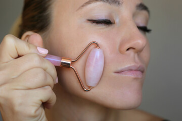Beautiful woman using pink Jade rose Quartz facial Roller. Skin treatment.
