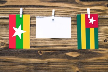 Hanging flags of Myanmar and Togo attached to rope with clothes pins with copy space on white note paper on wooden background.Diplomatic relations between countries.