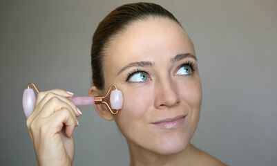 Beautiful woman using pink Jade rose Quartz facial Roller. Skin treatment.