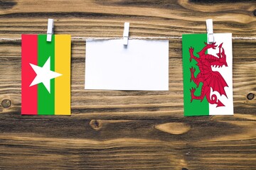 Hanging flags of Myanmar and Wales attached to rope with clothes pins with copy space on white note...