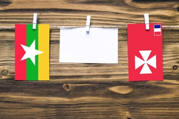 Hanging flags of Myanmar and Wallis And Futuna attached to rope with clothes pins with copy space on white note paper on wooden background.Diplomatic relations between countries.