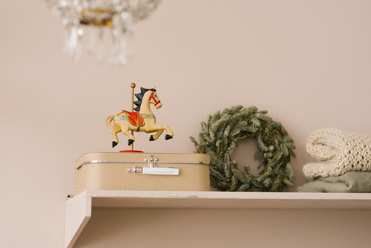 Wooden horse toy, a beige suitcase on a shelf and a Christmas wreath in the interior of a living room or dining room home