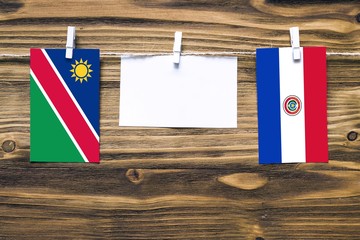 Hanging flags of Namibia and Paraguay attached to rope with clothes pins with copy space on white note paper on wooden background.Diplomatic relations between countries.