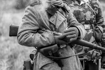 German Wehrmacht soldier in overcoat with a rifle in his hands and a cigarette. Black and white shot