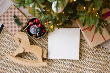 Photo book in a white cover with a lace cover from the skin, gifts and a wooden horse lie under a Christmas fir tree, top view