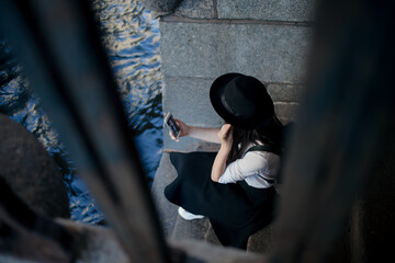 young woman in a hat and with a backpack walks in the city and uses a smartphone.