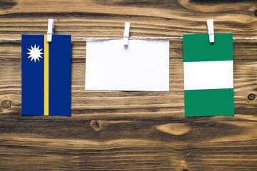 Hanging flags of Nauru and Nigeria attached to rope with clothes pins with copy space on white note...