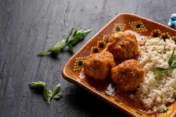 Mexican meatballs with red sauce and rice on dark background