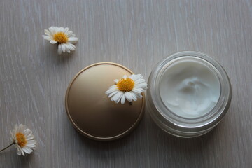 Obraz na płótnie Canvas Cosmetic cream in a jar and chamomile on the table.