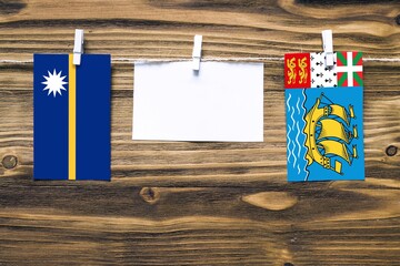 Hanging flags of Nauru and Saint Pierre And Miquelon attached to rope with clothes pins with copy space on white note paper on wooden background.Diplomatic relations between countries.