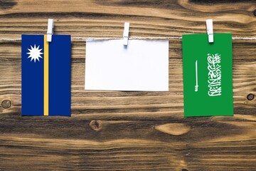 Hanging flags of Nauru and Saudi Arabia attached to rope with clothes pins with copy space on white...