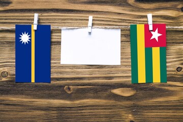 Hanging flags of Nauru and Togo attached to rope with clothes pins with copy space on white note paper on wooden background.Diplomatic relations between countries.