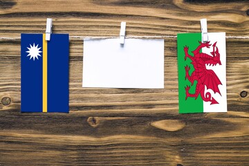 Hanging flags of Nauru and Wales attached to rope with clothes pins with copy space on white note...