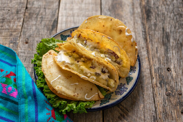 Mexican potato fried tacos with cheese and sour cream on wooden background