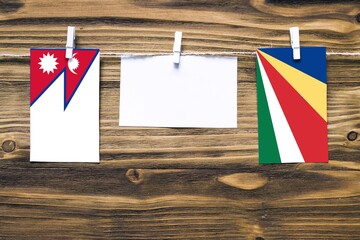 Hanging flags of Nepal and Seychelles attached to rope with clothes pins with copy space on white note paper on wooden background.Diplomatic relations between countries.