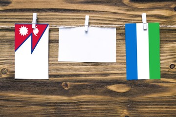 Hanging flags of Nepal and Sierra Leone attached to rope with clothes pins with copy space on white note paper on wooden background.Diplomatic relations between countries.